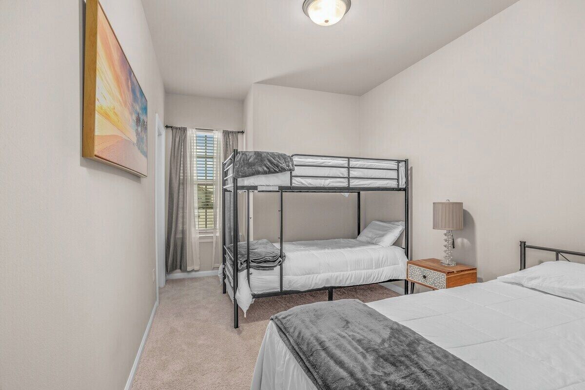 A bedroom with bunk beds, a bedside table with a lamp, and a window with curtains.