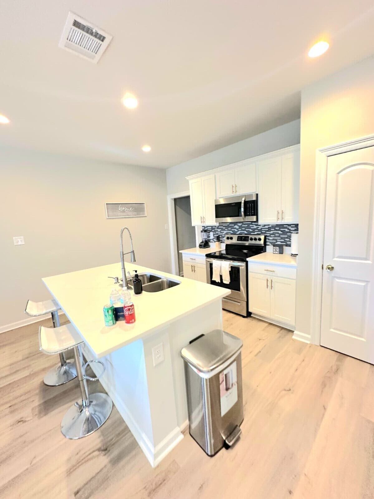 A modern kitchen with white cabinetry, stainless steel appliances, and a central island with bar stools.