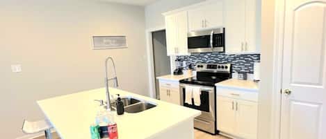 A modern kitchen with white cabinetry, stainless steel appliances, and a central island with bar stools.
