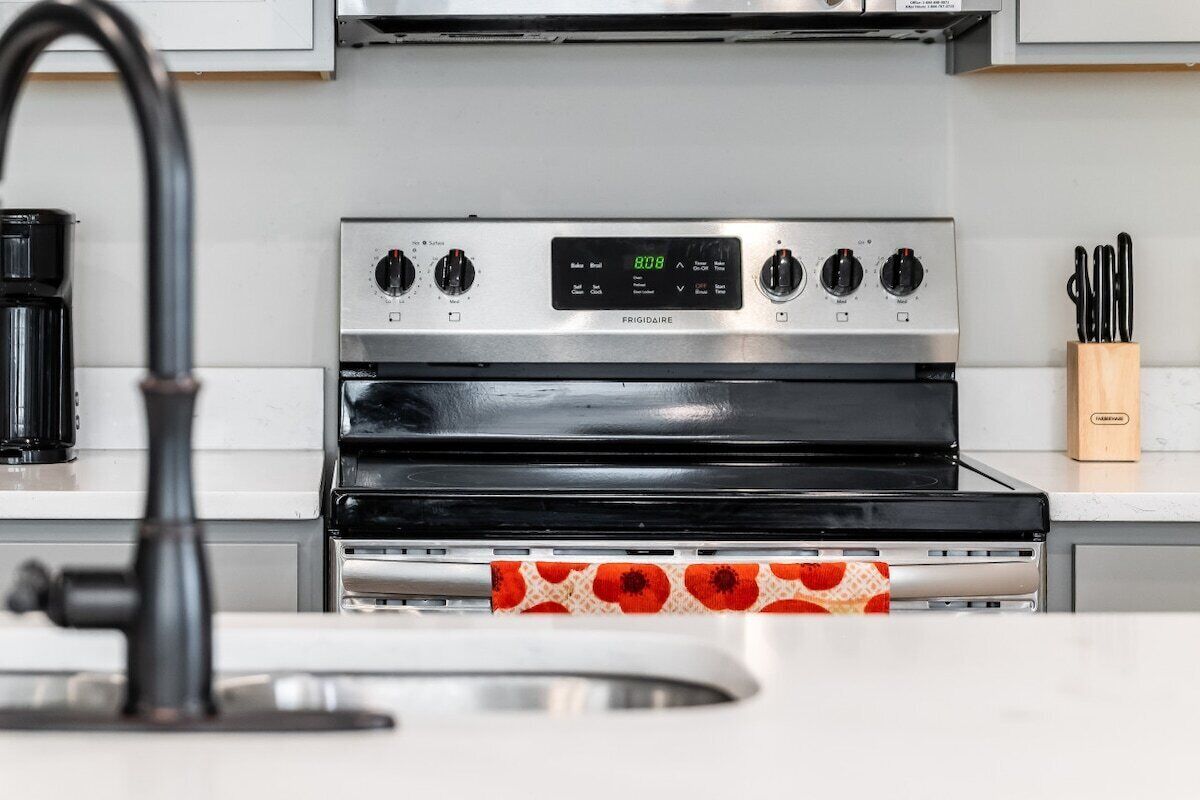 Una cocina con estufa de acero inoxidable, un reloj digital y una cafetera.