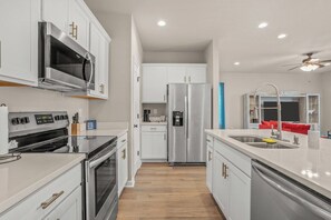 A modern kitchen with white cabinetry, stainless steel appliances, and a central island with a sink. - Serene Oasis for Deep Relaxation Near LSU - CL5628 (Baton Rouge)