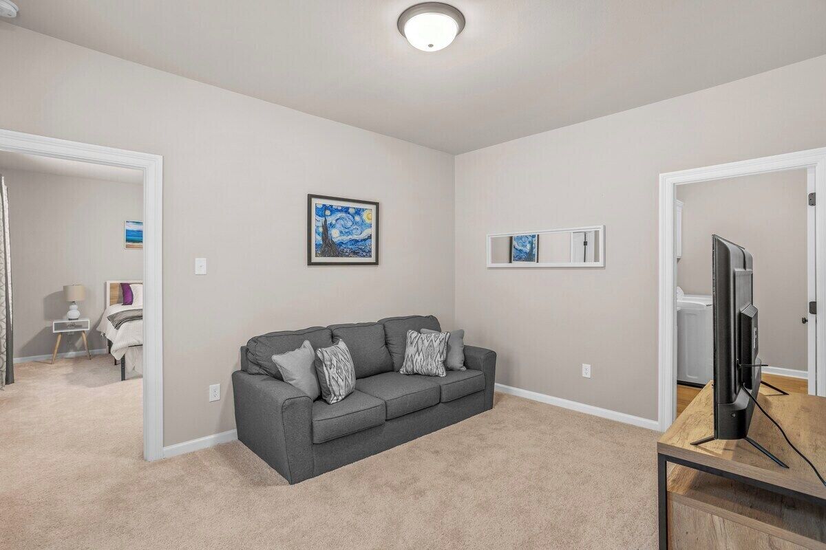 A living room with a grey sofa, a flat-screen TV on a wooden stand, and artwork on the walls.