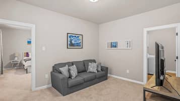A living room with a grey sofa, a flat-screen TV on a wooden stand, and artwork on the walls.