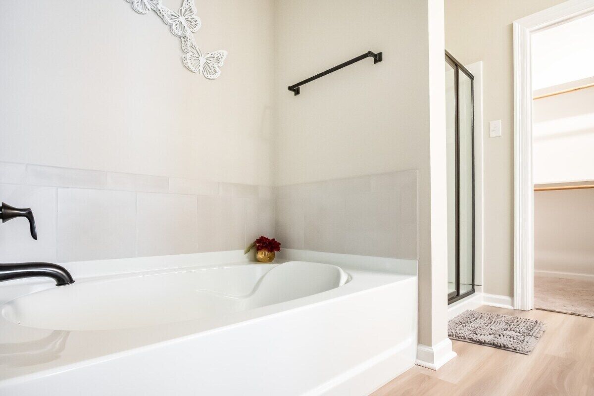 Un baño moderno con una bañera blanca, un perchero negro y una cabina de ducha de cristal.