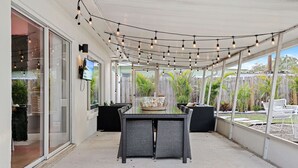 Un patio couvert avec une table et des chaises, des guirlandes lumineuses et un téléviseur fixé au mur.