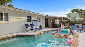 Une piscine avec des jeux gonflables, des chaises longues et un espace patio couvert.
