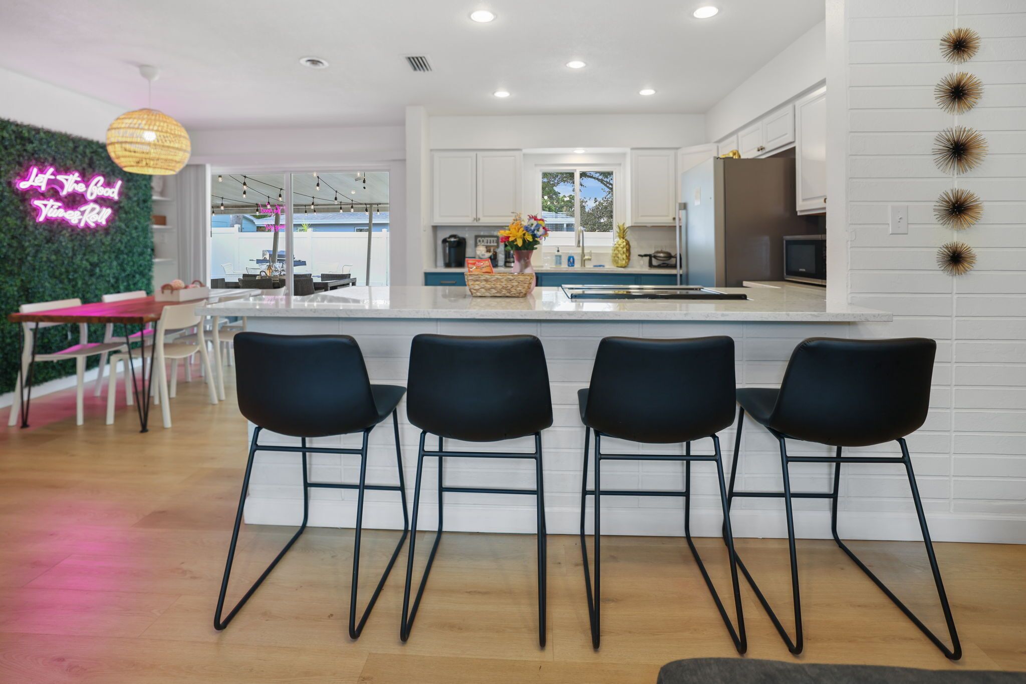 A modern kitchen with white cabinets, a central island with bar stools, and a neon sign on the wall.