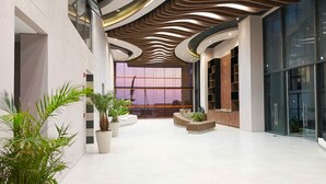 Un hall d’entrée spacieux au design moderne, avec un plafond incurvé, de grandes fenêtres et des plantes en pot.