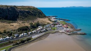 An aerial view of a coastal town with houses along the beach, a road curving through the town, and a pier extending into the sea. - Poet's Cottage Stanley (Stanley)