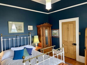 A bedroom with a white metal bed frame, a wooden wardrobe, and a door. - Poet's Cottage Stanley (Stanley)