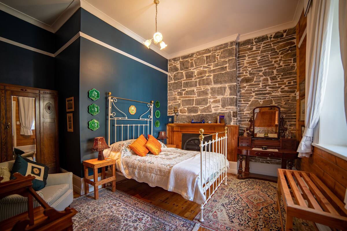 A bedroom with a stone wall, a bed with a white canopy, a wooden bench, and a fireplace.