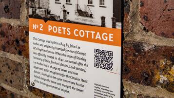 A historical plaque on a brick wall, detailing the Poets Cottage, a building with a white facade and multiple chimneys, indicating its historical significance and architectural style.