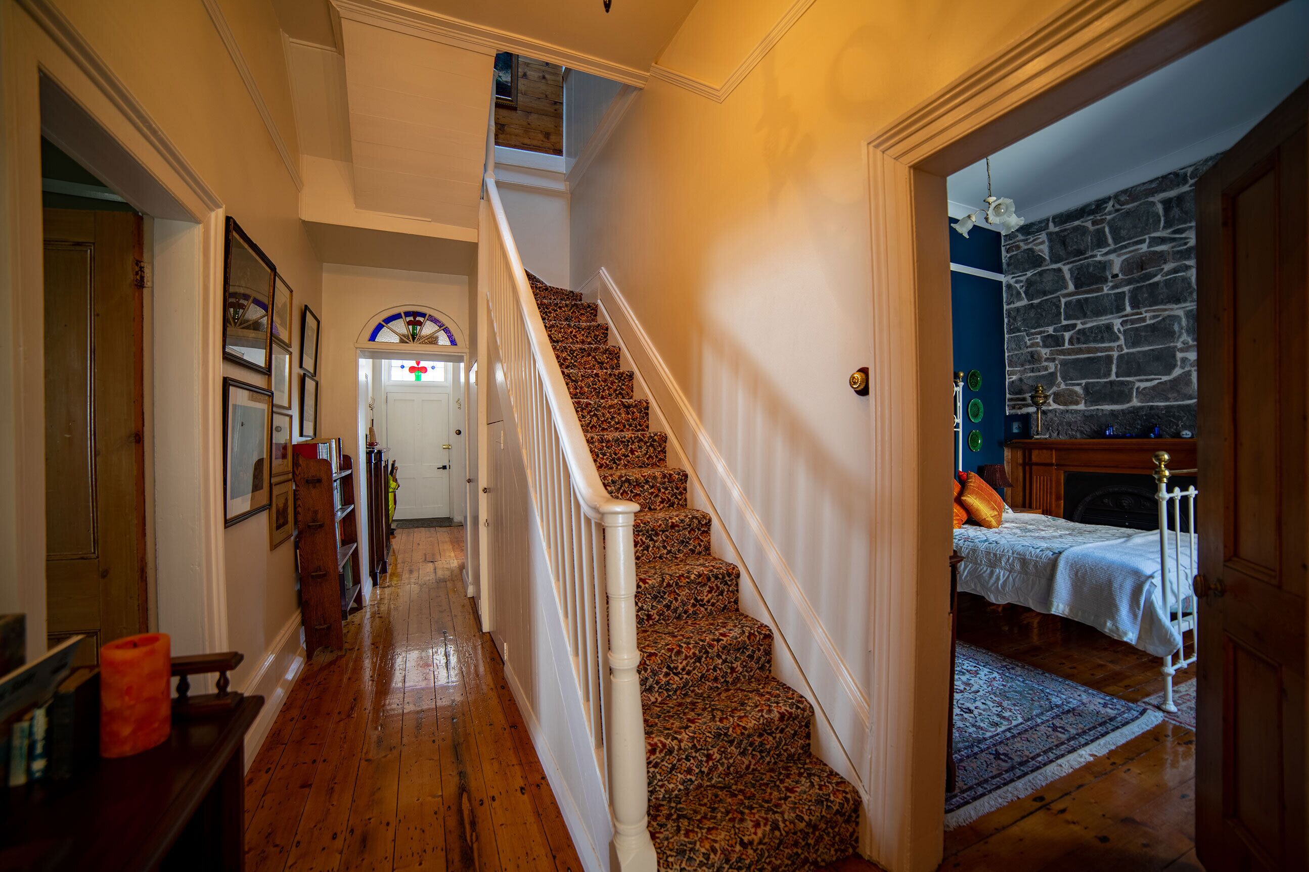 Uma escadaria com degraus revestidos em carpete leva a um quarto com parede de pedra e uma cama.