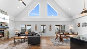 A spacious loft-style living area with a fireplace, a black leather sofa, a dining table with chairs, and a kitchen island. - Lake View Getaway with Hot Tub, Arcade, Indoor Community Pool & Free Silver Dollar Tickets (Hollister)