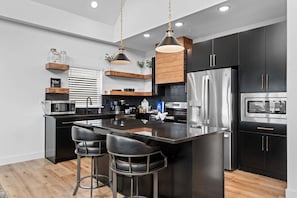 A modern kitchen with a central island, stainless steel appliances, and black cabinetry.