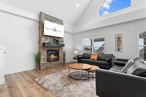 A modern living room with a stone fireplace, a black leather sofa, a round coffee table, and a large window with blinds.