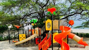 Un parque infantil con toboganes y estructuras para escalar, rodeado de árboles y suelo arenoso.