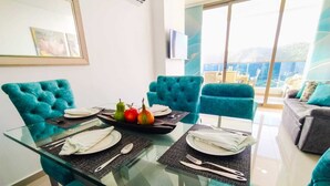 Un comedor con mesa de vidrio, sillas tapizadas en color aguamarina y vista al mar a través de amplias ventanas.