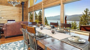 A wooden cabin with a dining area set for four, large windows, and a view of a lake and mountains. - Ski, Swim, Relax at Whitefish Lake | Stunning Views of Whitefish Lake (Whitefish)