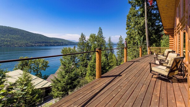 A wooden deck with outdoor furniture overlooking a lake and forested hills. - Ski, Swim, Relax at Whitefish Lake | Stunning Views of Whitefish Lake (Whitefish)