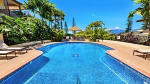 A swimming pool with lounge chairs and a thatched umbrella, surrounded by tropical plants and a clear blue sky.