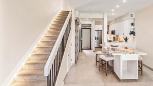 A modern kitchen with a central island, a staircase, and a dining area with bar stools.