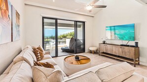 A modern living room with a large flat-screen TV, a sofa, a coffee table, and a sliding glass door leading to an outdoor area.
