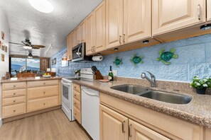 A kitchen with wooden cabinets, a granite countertop, a double sink, and a microwave. - Celebrate in style with stunning Oceanfront views (Wailuku)