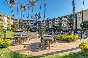 A courtyard with outdoor seating, palm trees, and a multi-story building in the background. - Celebrate in style with stunning Oceanfront views (Wailuku)