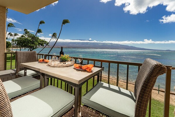 Un coin repas avec vue sur l’océan, des meubles en osier et une table dressée avec une bouteille et un verre.