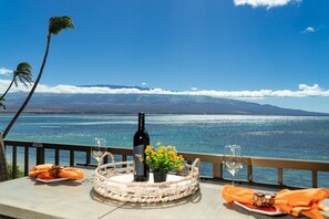 Une table avec une bouteille de vin, un verre et une assiette de nourriture, le tout placé devant un paysage de mer bleue et de montagnes lointaines.