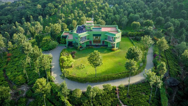 Une grande maison moderne, entourée d’une végétation luxuriante et de collines.