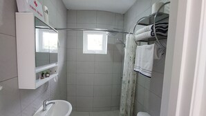Un baño con ducha, inodoro, lavamanos y espejo.