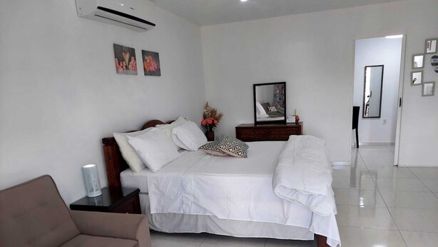 Un dormitorio con cama, mesita de noche, cómoda, espejo y una puerta que da a otra habitación.