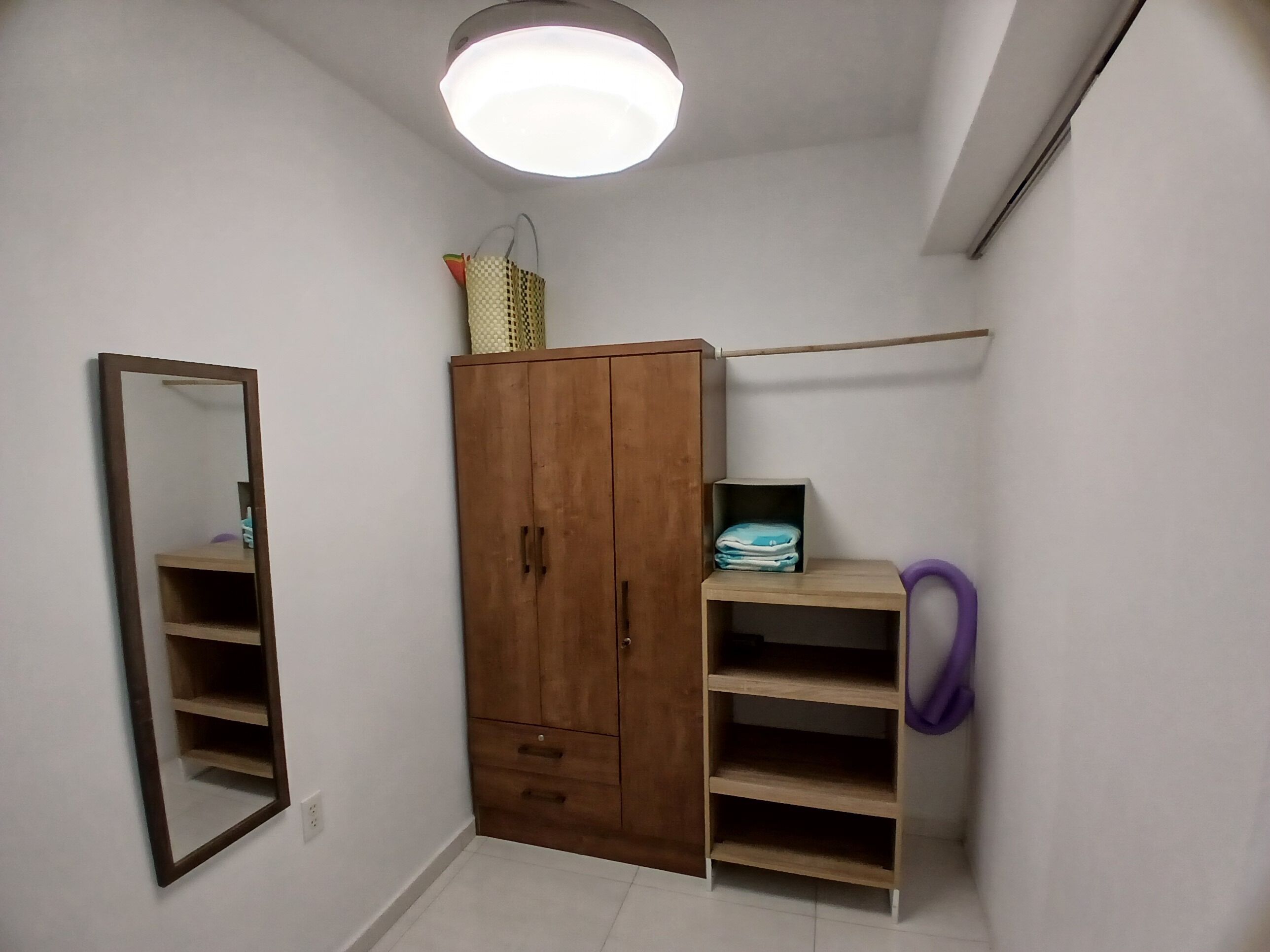 A room with a wardrobe, a mirror, a shelf with folded clothes, and a hanging purple item.