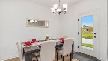 A dining area with a dark wooden table, beige upholstered chairs, and a chandelier.