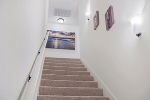 Eine Treppe mit Teppichstufen führt zu einer Zwischenebene, auf der sich ein Gemälde und Wandleuchten befinden.