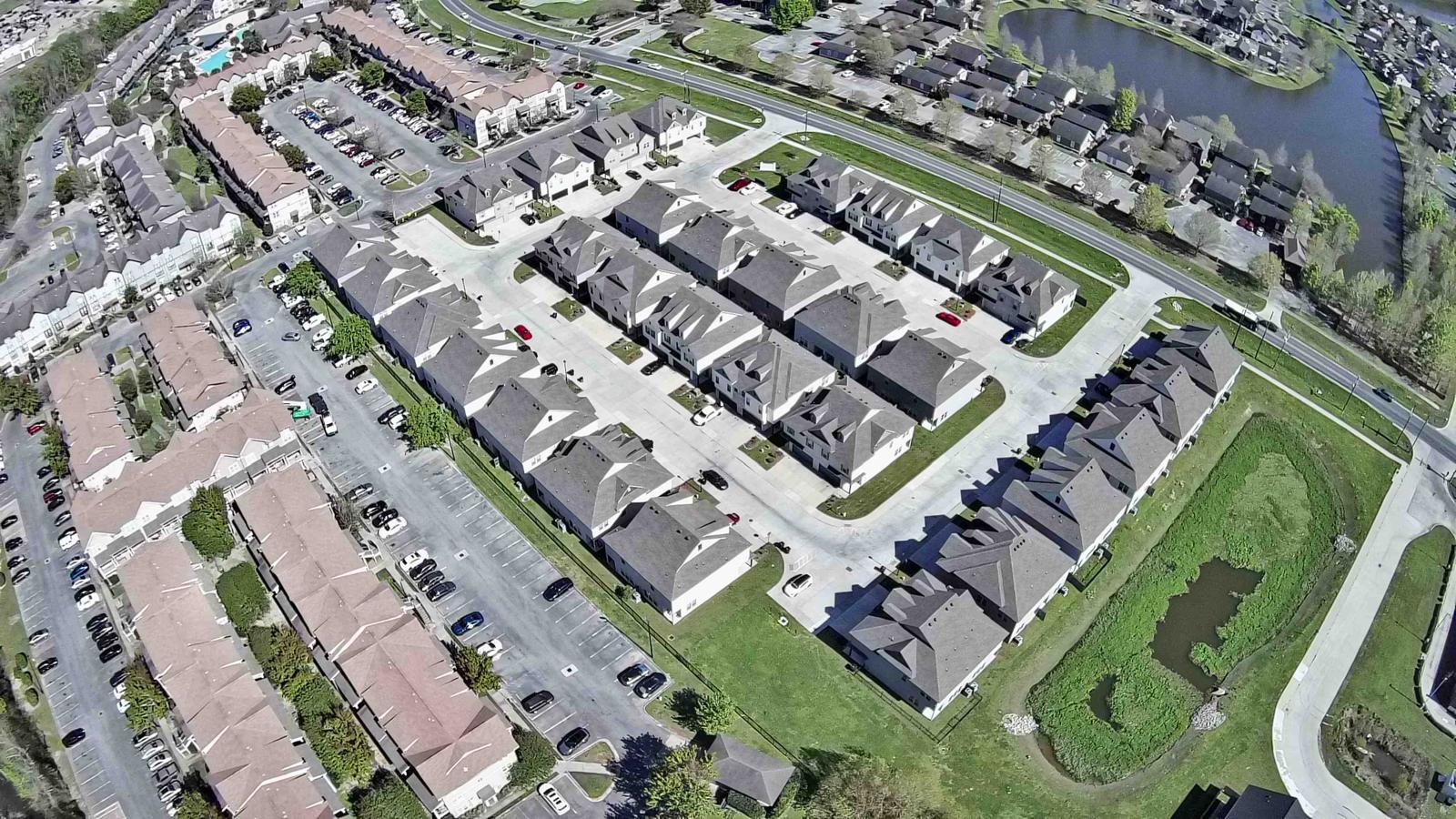 Vue aérienne d’un quartier résidentiel composé de maisons individuelles, une rue principale et une  étendue d’eau.