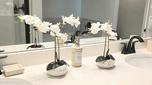 A bathroom with a white sink, a mirror, and three orchid vases. - Peaceful Bayou Escape Close to LSU Campus - CL5626 (Baton Rouge)