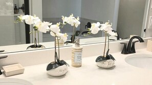 A bathroom with a large mirror, two sinks, and three orchid vases.