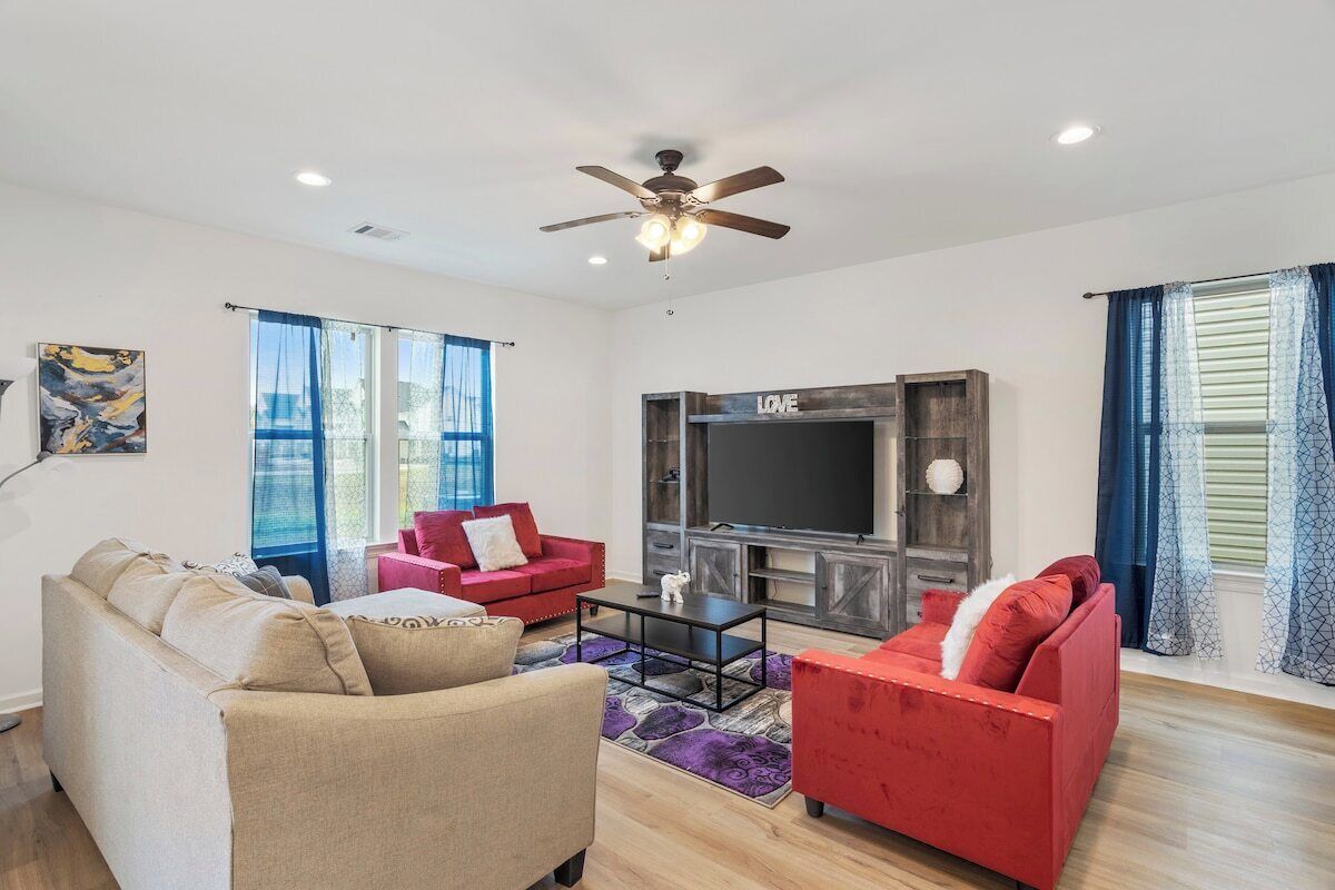 A living room with a sofa, red chairs, a TV, and a ceiling fan.
