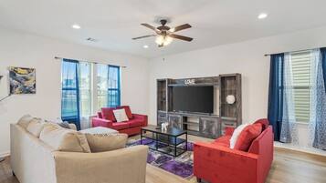 A living room with a sofa, red chairs, a TV, and a ceiling fan.