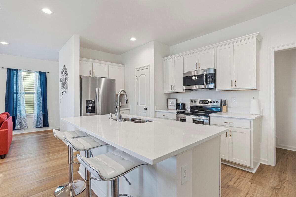 Una cocina moderna con armarios blancos, electrodomésticos de acero inoxidable y una zona de bar con taburetes.