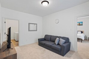 Ein Wohnzimmer mit grauem Sofa, einem Flachbildfernseher, einer Uhr und einem gerahmten Bild an der Wand.