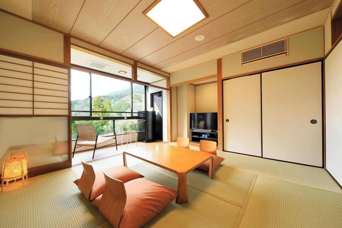 A traditional Japanese-style room with tatami flooring, a low table, cushions, a television, and sliding doors.