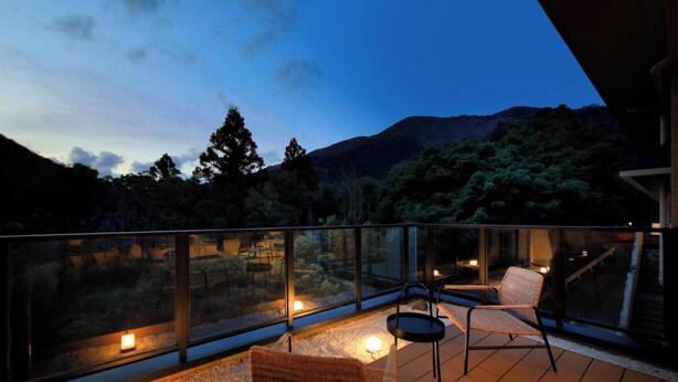 A balcony with two wicker chairs, a small table, and a glass railing overlooking a mountainous landscape. - Hakone Suisen (Hakone)