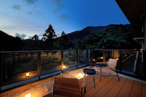 A balcony with two wicker chairs, a small table, and a glass railing overlooking a mountainous landscape. - Hakone Suisen (Hakone)