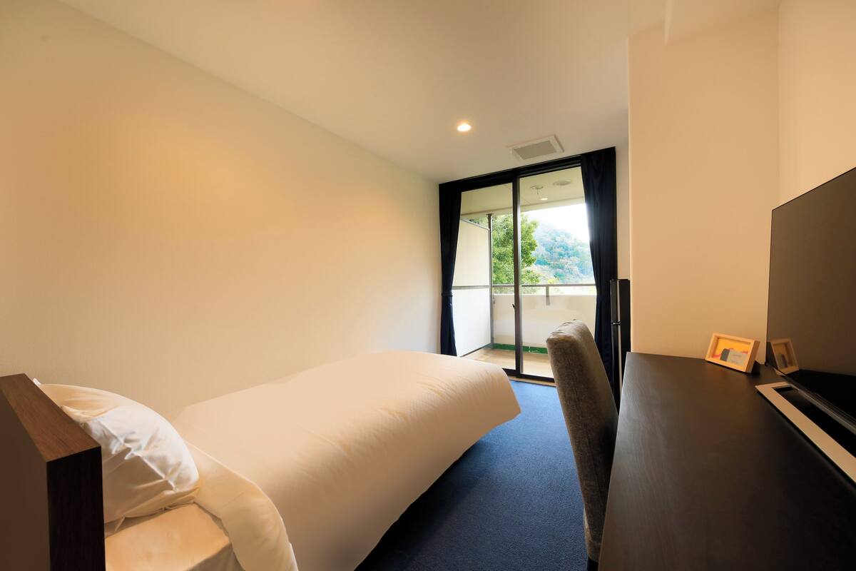 A modern hotel room with a bed, a desk, and a view of the outdoors.