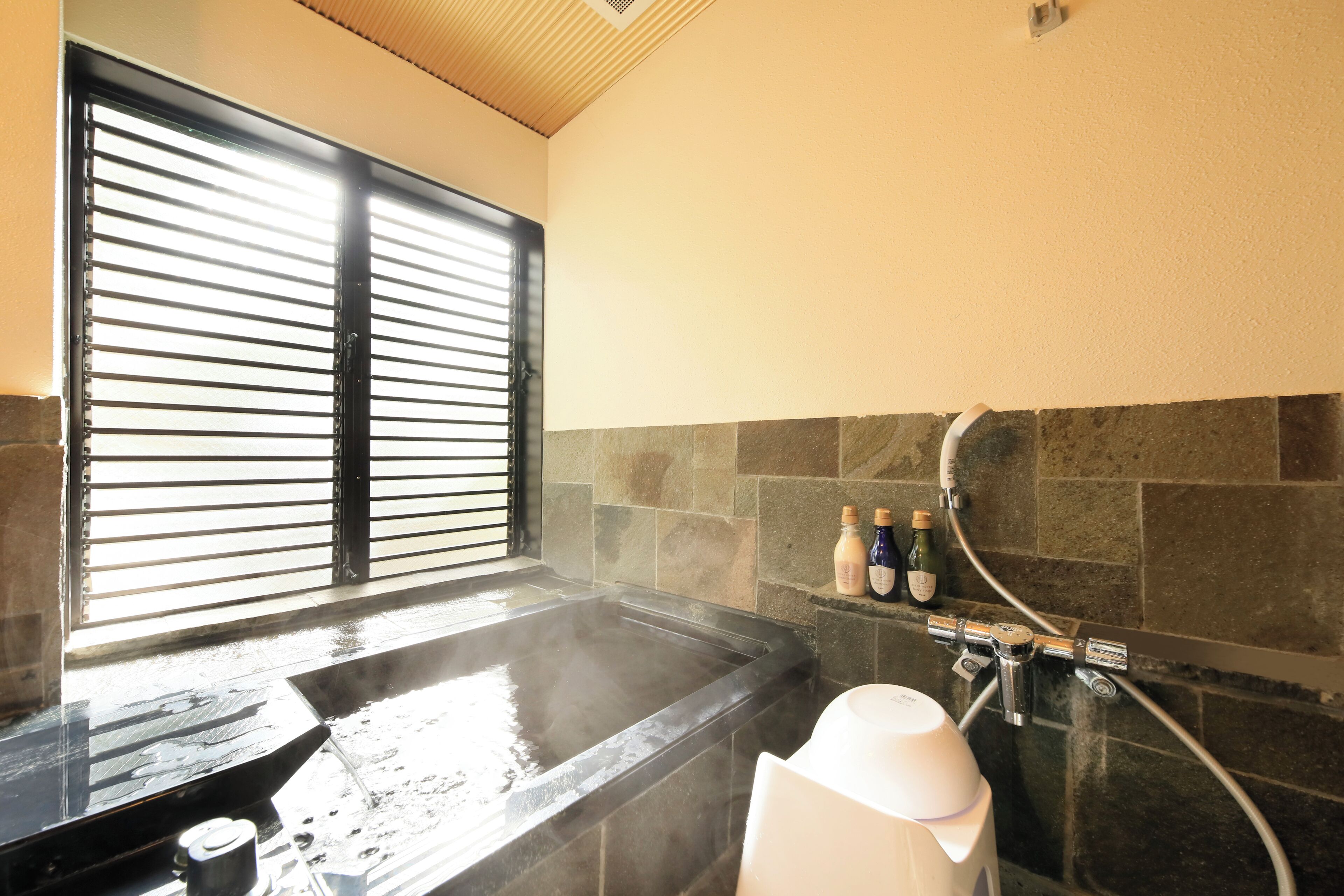 Baño de vapor con ventana, paredes de piedra y zona de ducha con botellas y un grifo.