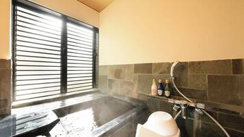 Baño de vapor con ventana, paredes de piedra y zona de ducha con botellas y un grifo.